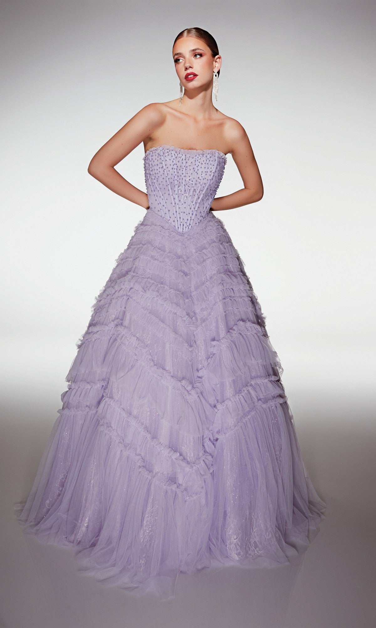 A woman in the Alyce 62208 long lilac prom dress with a strapless beaded bodice and layered tulle ruffle skirt stands against a plain background.